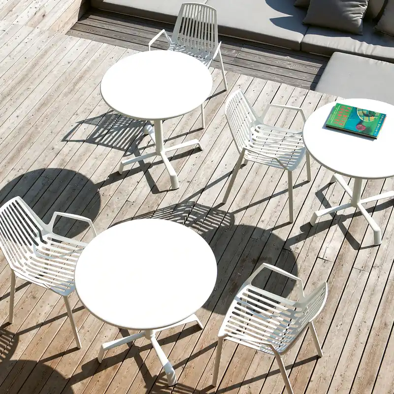 Fast Rion white aluminum chairs with wire backs around round white tables on a wooden deck, seen from above
