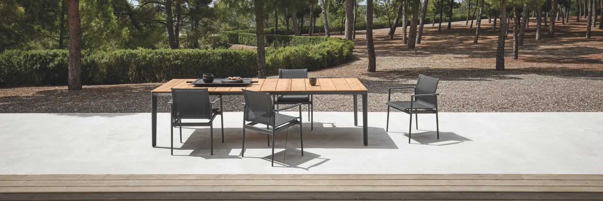 Gloster 180 chairs around a teak-topped dining table on a terrace at the edge of a pine wood