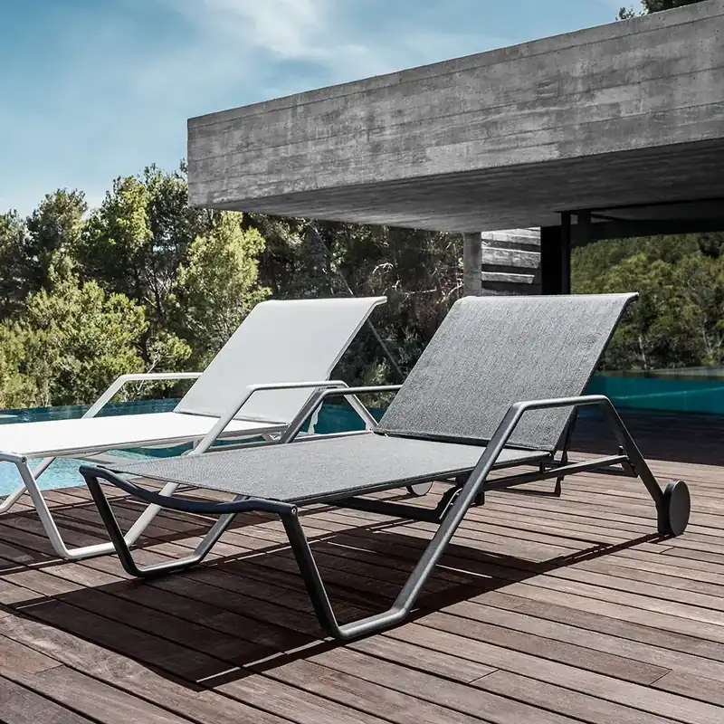 Gloster 180 sun loungers with sling seats on a wooden deck beside a concrete house, pine trees behind