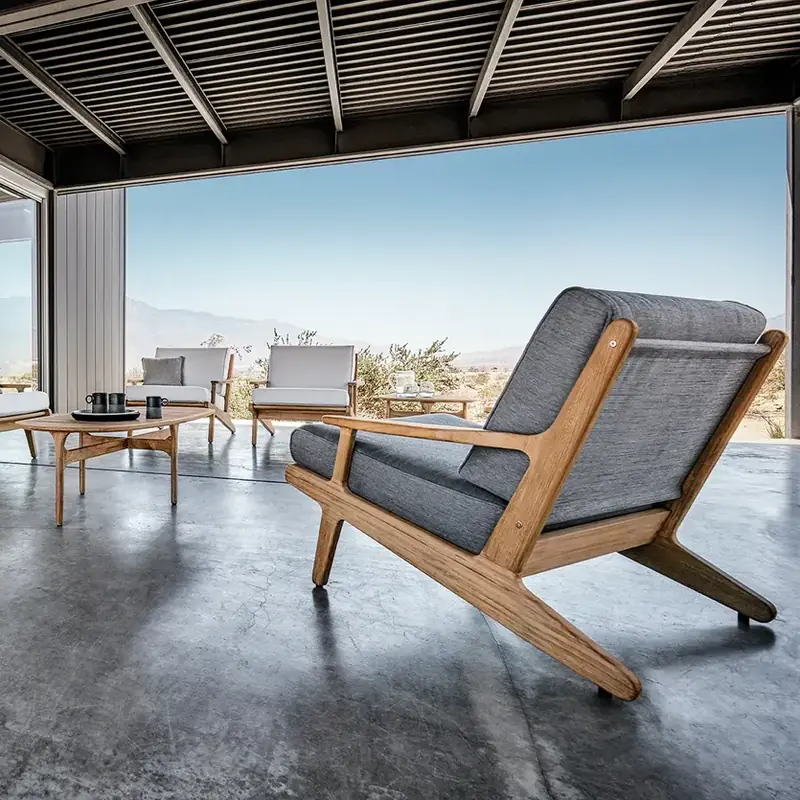 Gloster Bay teak lounge chair with a dark sling seat on a covered terrace, next to a fire bowl