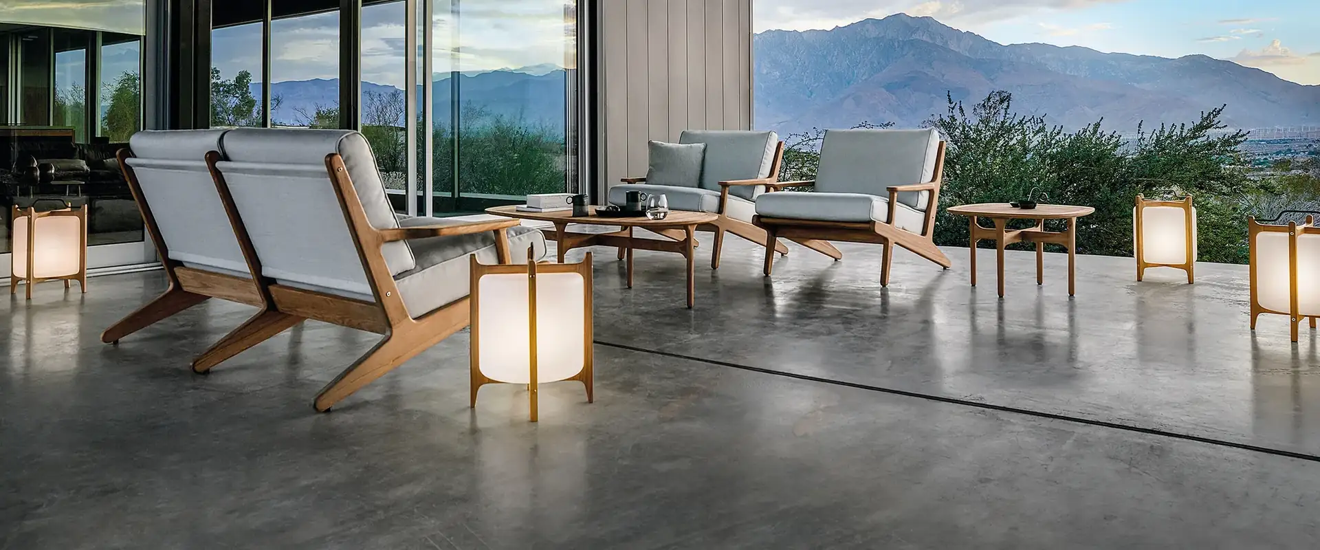 Gloster Bay teak lounge chairs with white cushions on a polished concrete terrace, with a mountain range beyond