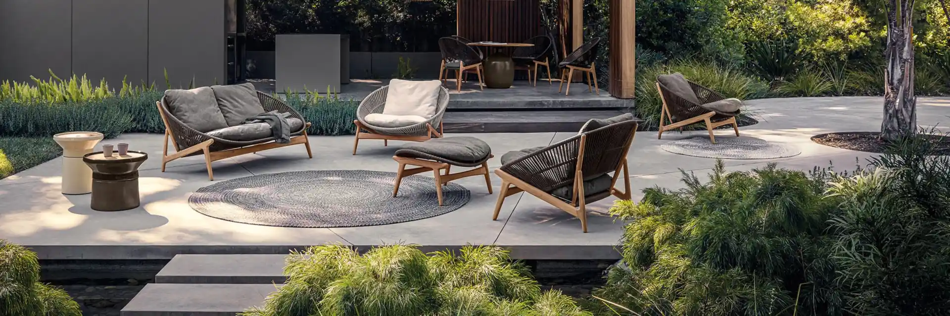 Gloster Bora sofa and lounge chairs with rope-woven backs around low tables on a stone terrace in front of a garden pavilion