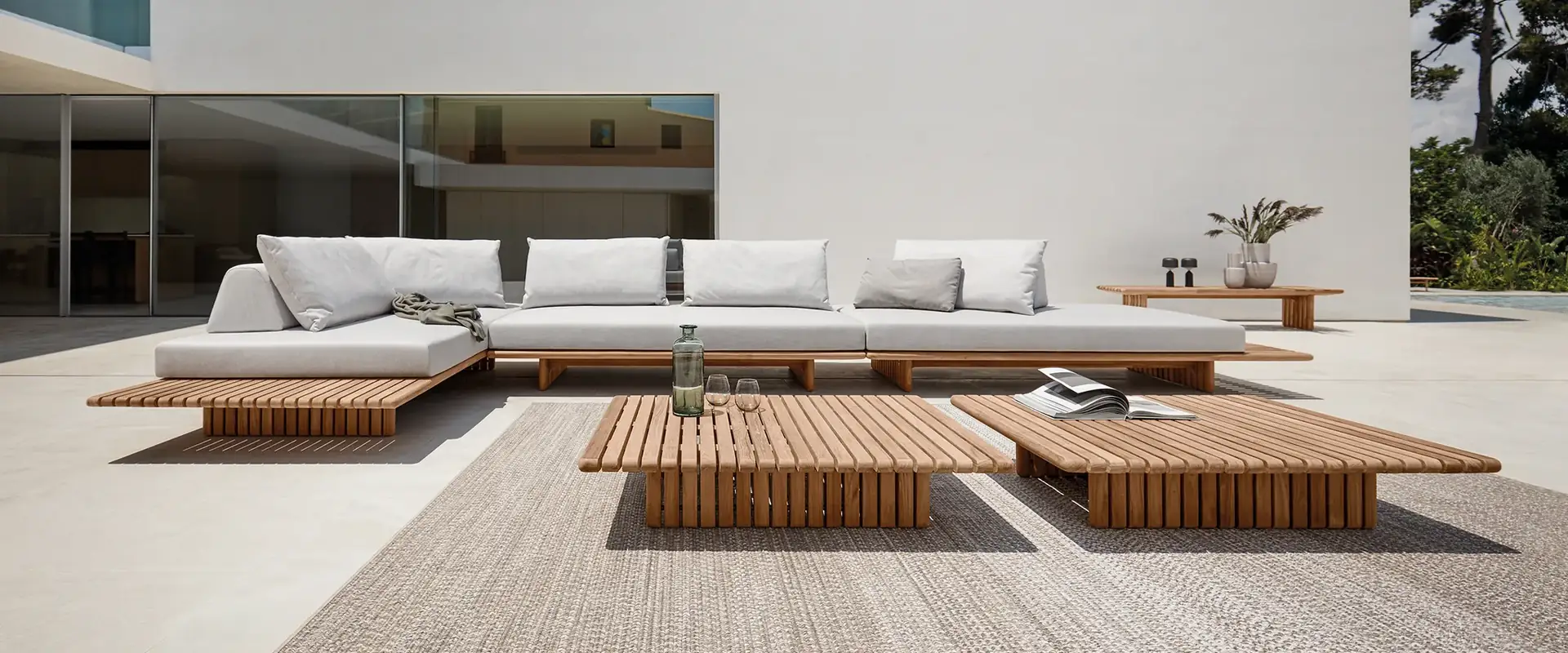 Gloster Deck low modular sofa with white cushions and slatted teak tables on a pale terrace in front of a white modern house