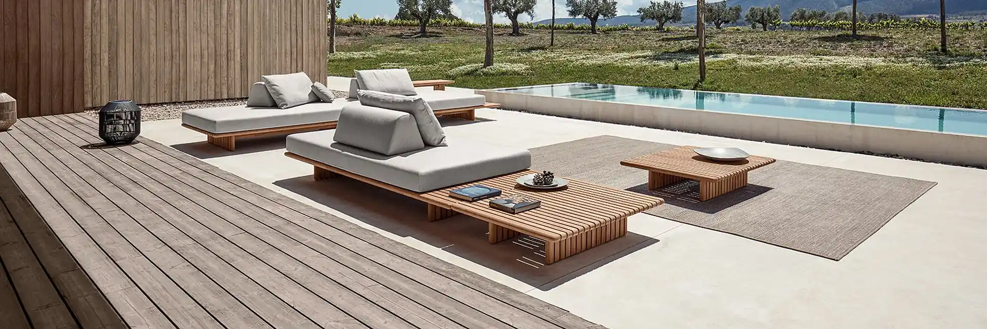Gloster Deck modular platform seating on a timber deck beside a pool, with young trees and hills beyond