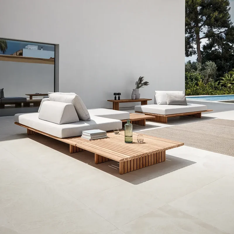 Gloster Deck modular sofa with a slatted teak coffee table on a white terrace under a cloudy blue sky
