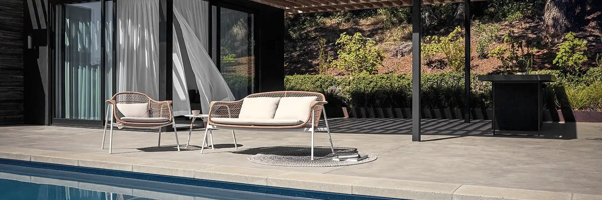 Gloster Fresco lounge chairs under the pergola of a dark pool house, reflected in the pool