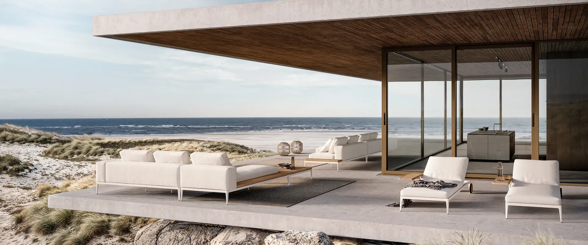 Gloster Grid modular sofas with white cushions on the deck of a flat-roofed beach house among sand dunes