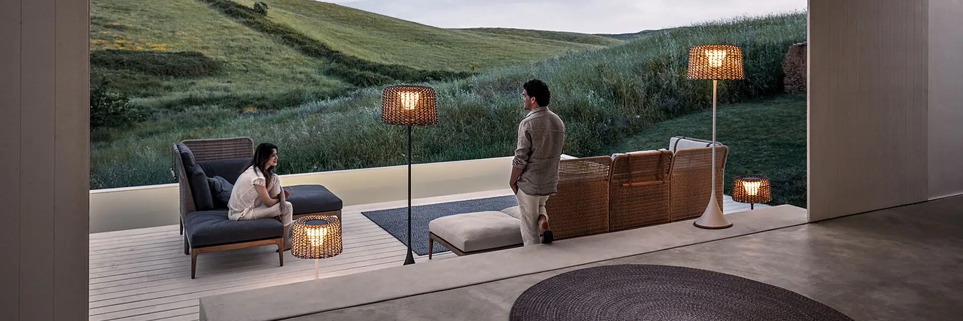 Two people sitting on Gloster Lima lounge furniture on a covered terrace overlooking green hills