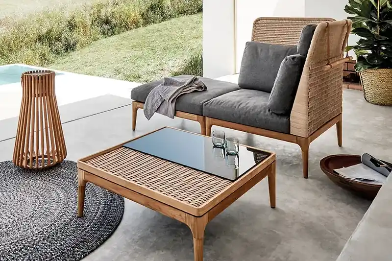 Gloster Lima teak lounge chair with a woven back and grey cushions beside a teak coffee table and a lantern on a concrete terrace