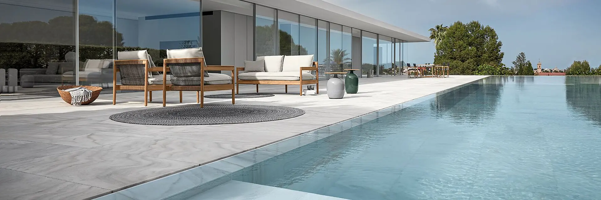 Gloster Saranac lounge furniture on the terrace of a glazed house beside a long pool