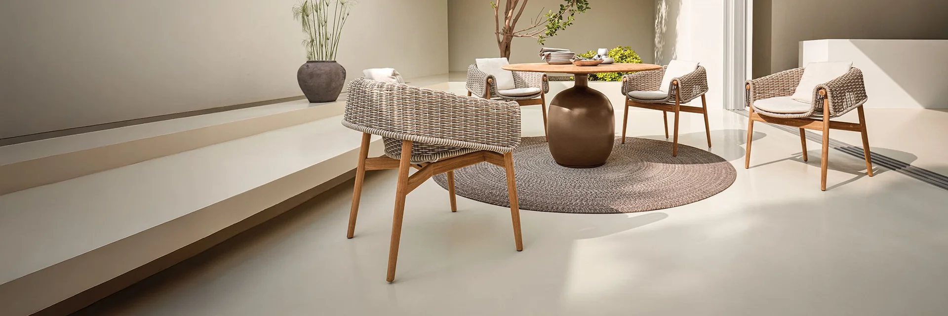 Gloster Wrap woven chairs around a round table in a white courtyard with a young tree