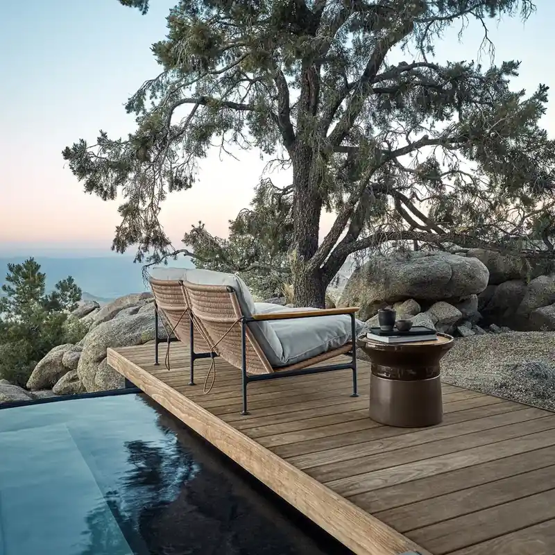 Gloster Zenith sofa with cream cushions on a wooden deck beside a dark pool, under an old tree overlooking the sea