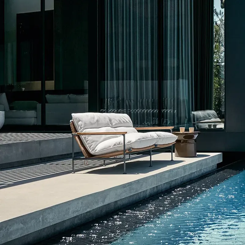 Gloster Zenith sofa with white cushions on a terrace beside a blue pool, under a glass-walled house