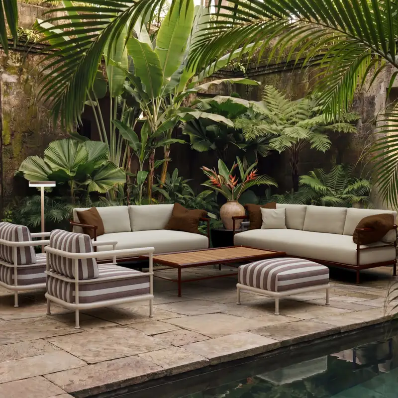 Kettal Alize sofas, armchairs and a striped pouf around a low table in a courtyard with palms and tropical plants beside a pond