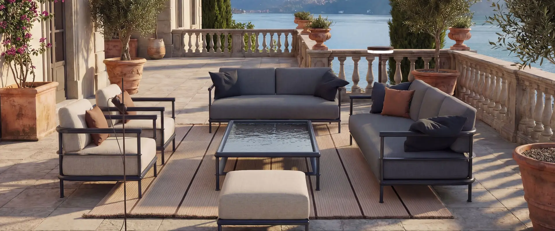 Kettal Alize sofas and armchairs in dark fabric around a coffee table on a stone terrace with cypress trees, overlooking a lake and mountains