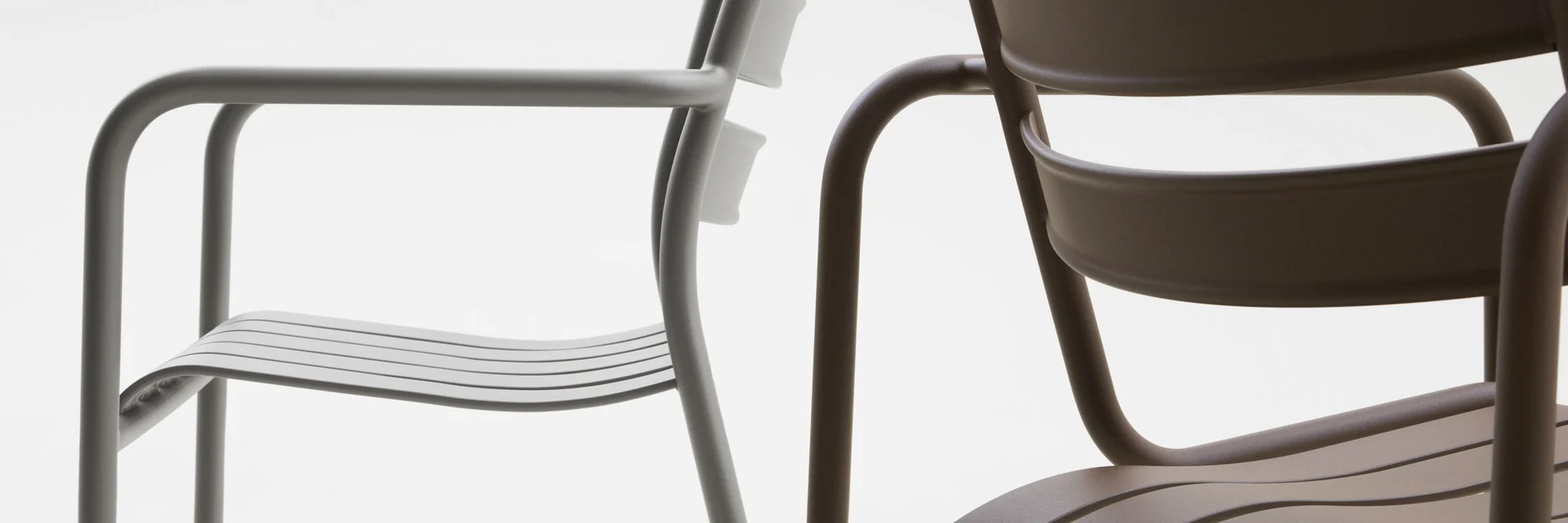 Close view of two Kettal Atlantic chairs with tubular frames and slatted seats, one grey and one dark brown