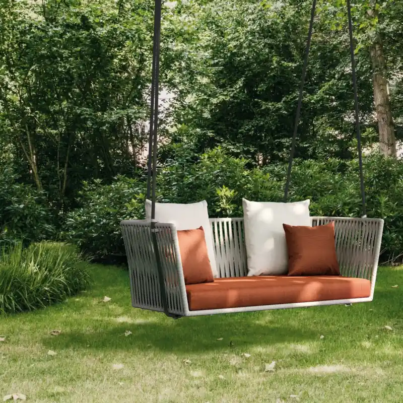Kettal Bitta two-seater hanging sofa with orange cushions suspended from a large tree on a green lawn