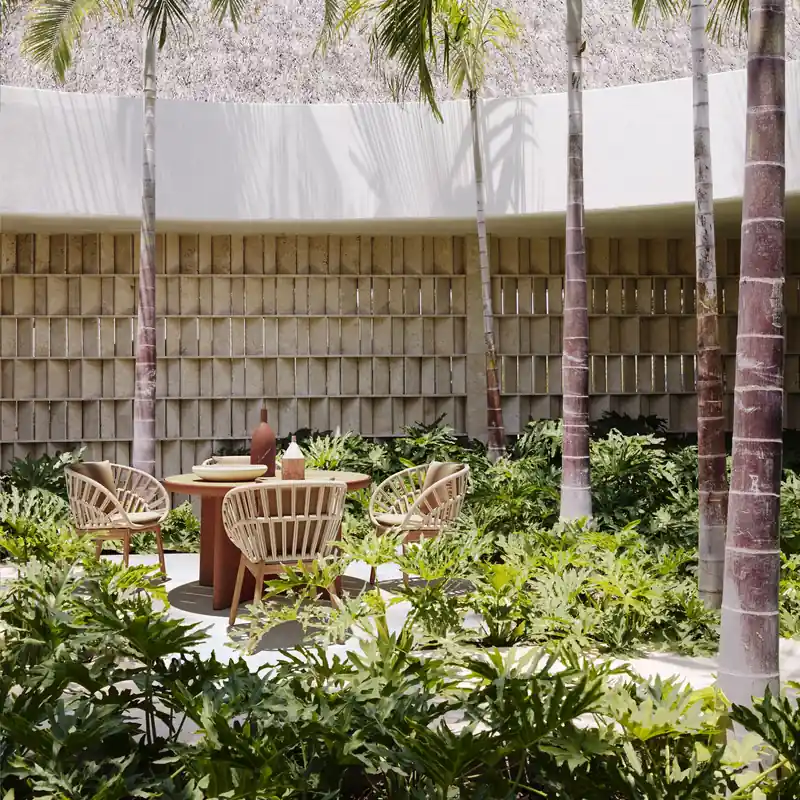 Kettal Cala rope armchairs around a round terracotta table in a garden of palm trees and tropical plants, in front of a lattice wall