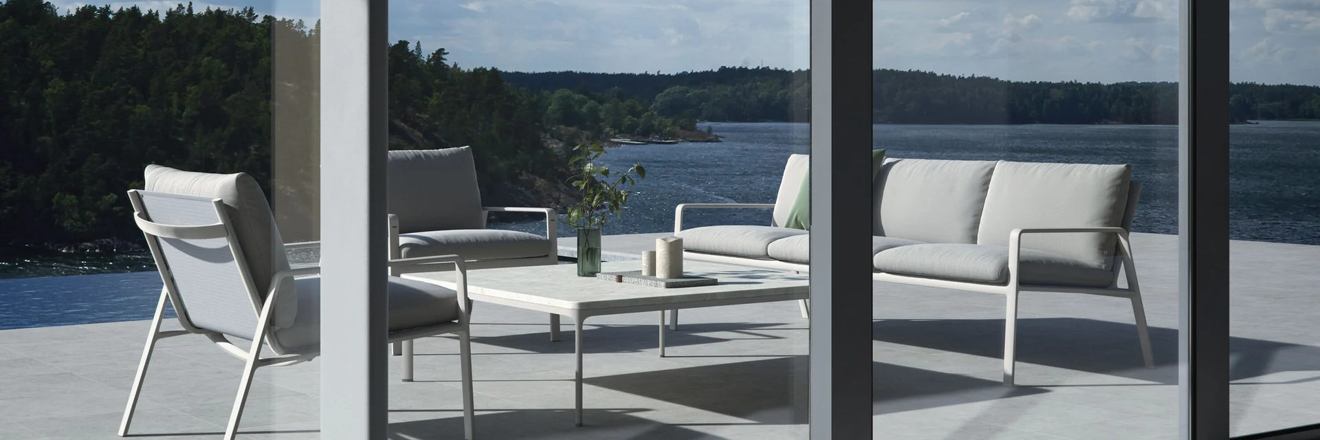 Kettal Park Life sofa, armchairs and low table on a terrace overlooking a lake, seen through tall glass panels