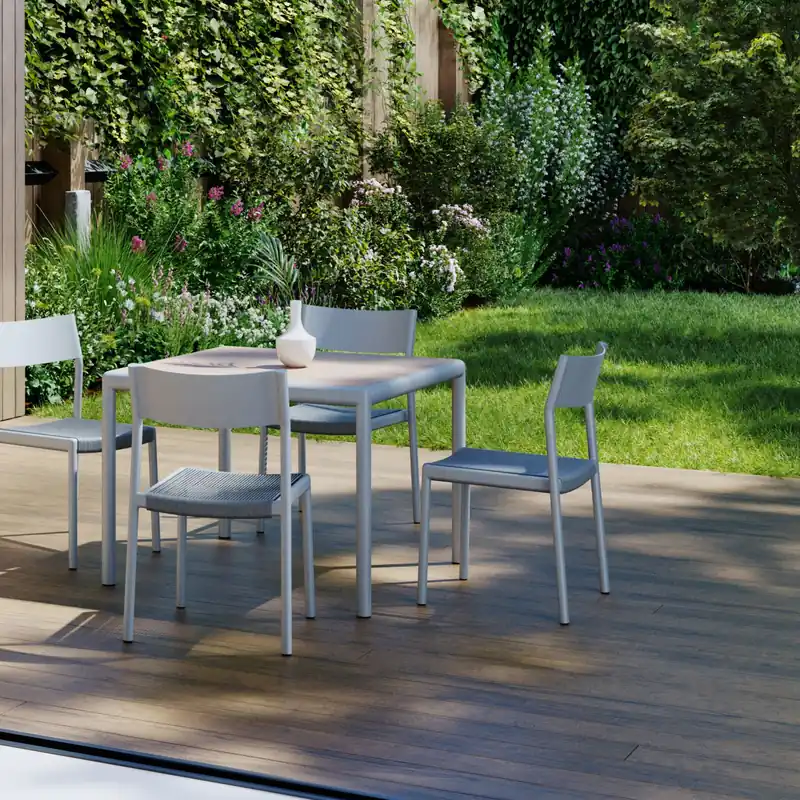 Kettal Passage aluminum chairs around a dining table on a wooden deck seen through a glass door, with a garden wall covered in plants