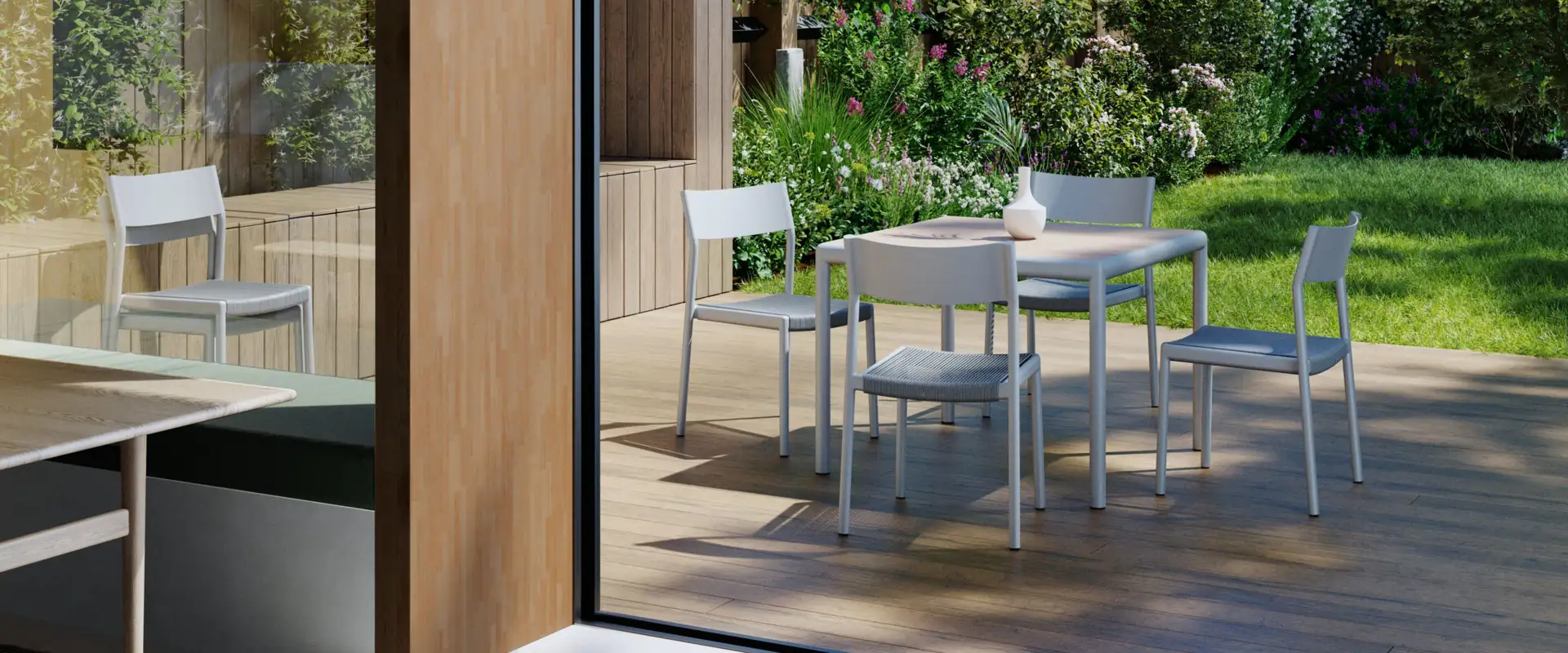 Kettal Passage aluminum chairs around a dining table on a wooden deck seen through a glass door, with a garden wall covered in plants