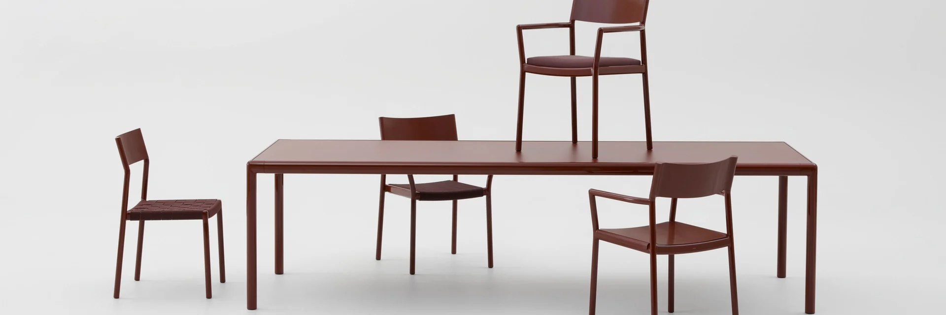 Kettal Passage dining table with matching chairs in dark red, against a pale studio backdrop
