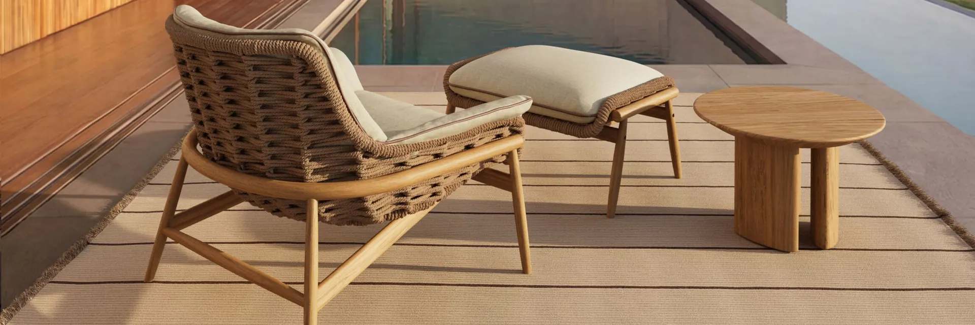 Kettal Tilos woven lounge chair with a footstool and side table on a timber deck beside a pool at dusk