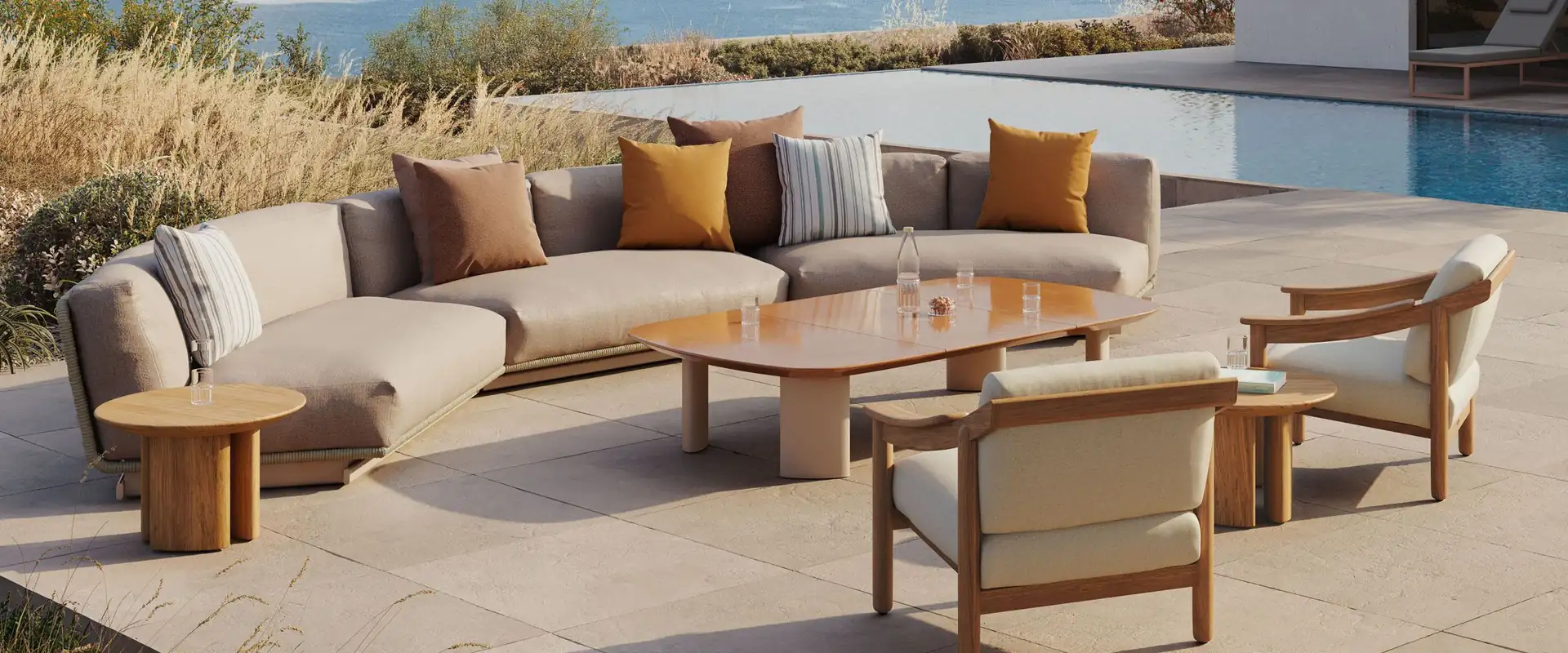 Kettal Tilos curved rope sofa with ochre cushions, low tables and teak armchairs on a stone terrace with a pool, overlooking the sea and islands