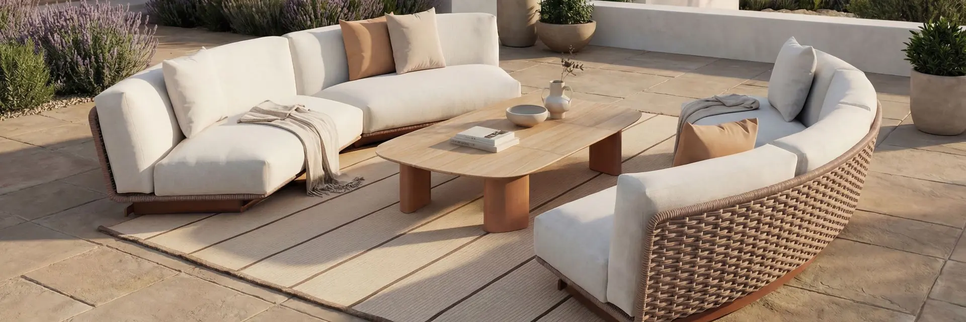 Kettal Tilos curved sofas in white with a low table on a stone terrace beside a white house, olive trees and the sea beyond