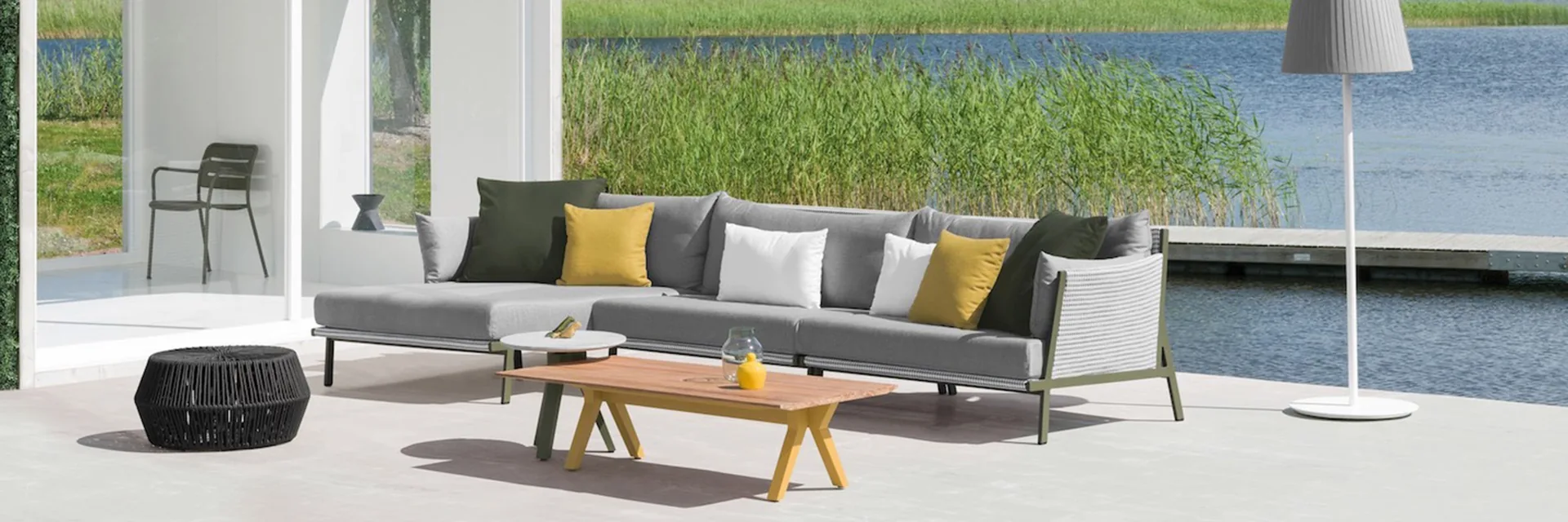Kettal Vieques modular sofa with colourful cushions on a deck beside a lake, next to a white pavilion