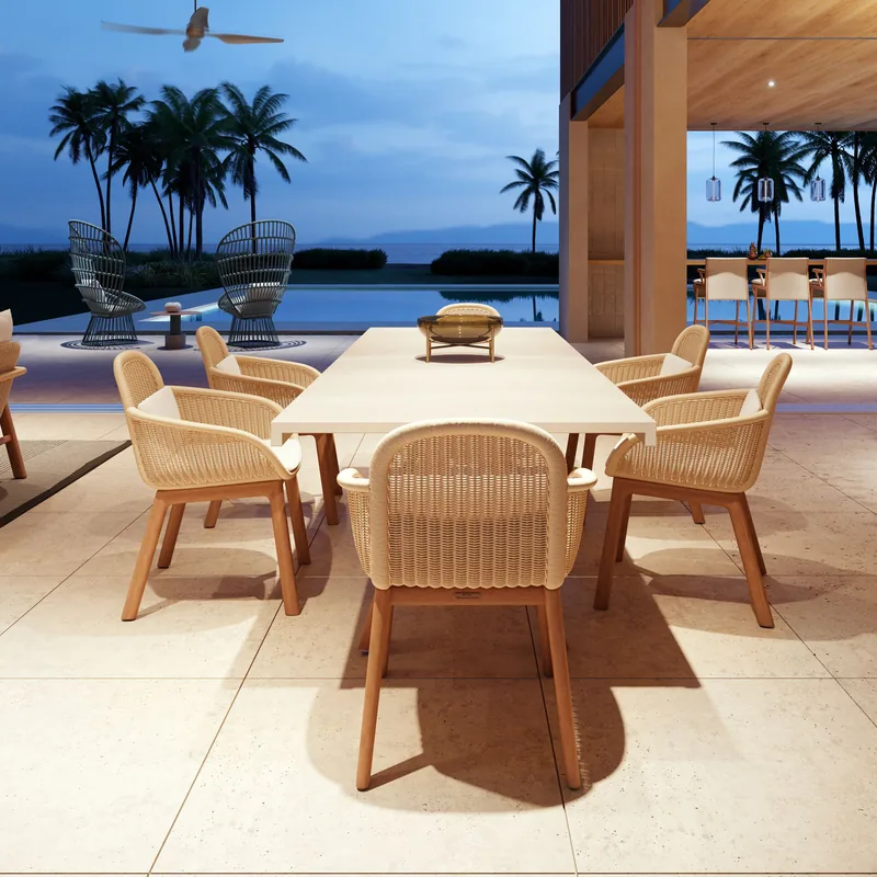 Kettal Vimini wicker dining chairs around a pale table on a covered terrace at dusk, with palm trees and the sea behind