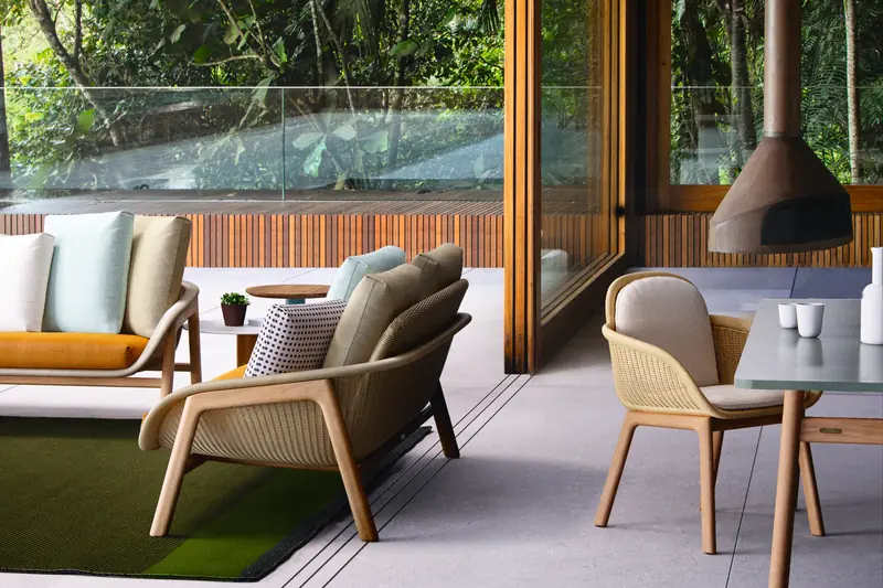 Kettal Vimini sofa and armchair with woven backs on a covered terrace with a hanging fireplace, open to a forest