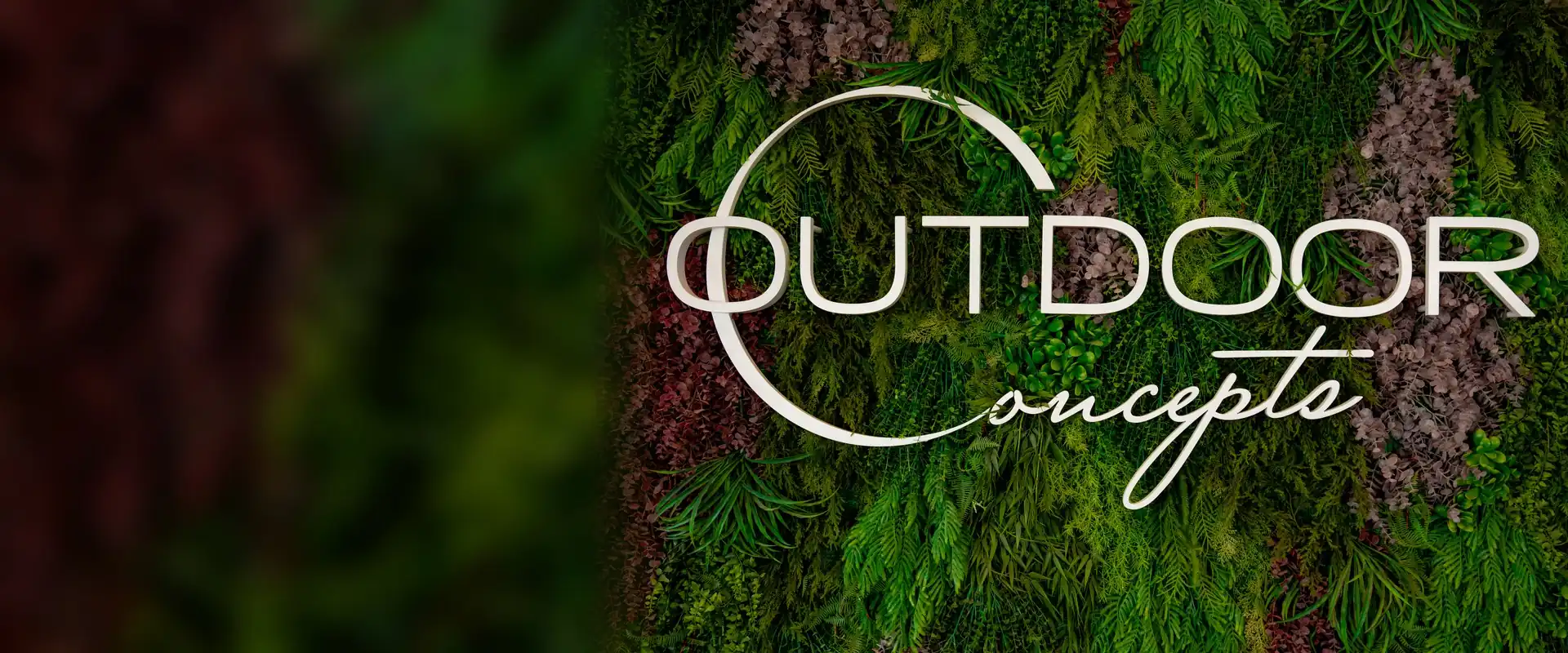 The Outdoor Concepts logo in white letters on a wall of green and burgundy plants in our Marbella showroom