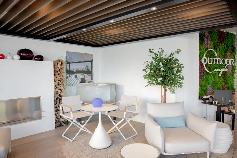 Folding chairs, a round table and lounge armchairs beside a bioethanol fireplace and the green Outdoor Concepts logo wall in the showroom