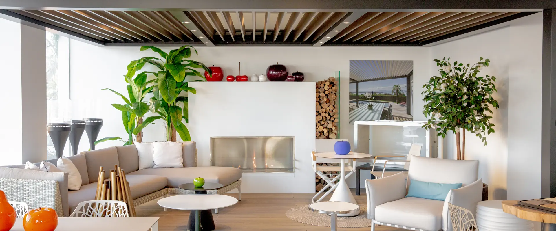 Outdoor lounge set under a louvred pergola in the Outdoor Concepts showroom, with a corner sofa, armchairs and a bioethanol fireplace