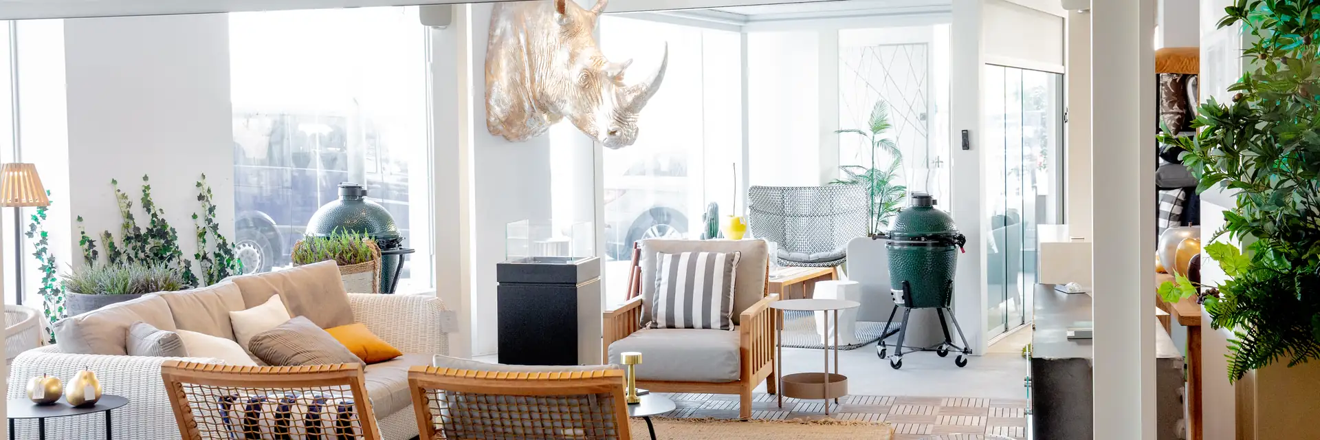 Lounge area in the Outdoor Concepts showroom with a woven sofa, teak armchairs and Big Green Egg kamados on display