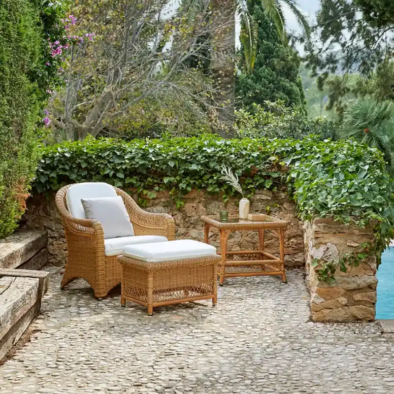Point Arena wicker armchair with white cushions and a matching footstool on a pebble terrace in a walled garden