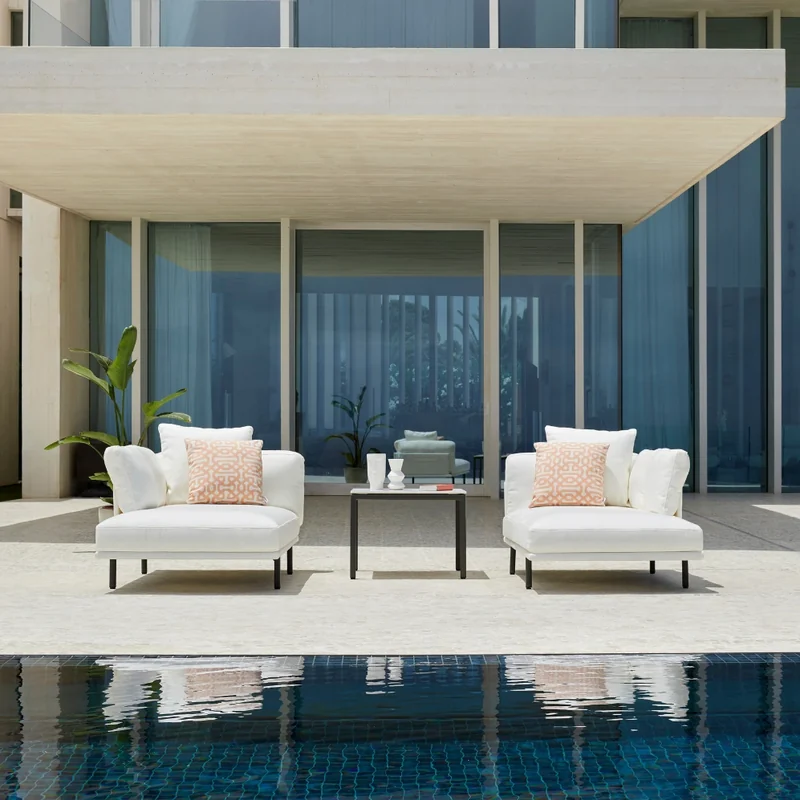 Two Point Long Island armchairs in white with a low table at the edge of a pool, under the canopy of a modern house