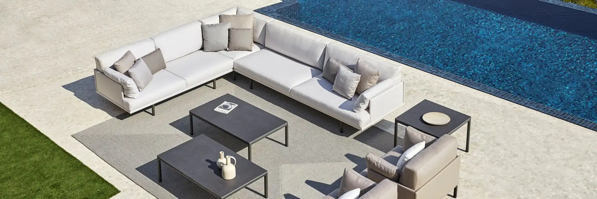 Point Long Island corner sofa and coffee tables on a stone terrace between a lawn and a dark-tiled pool, seen from above