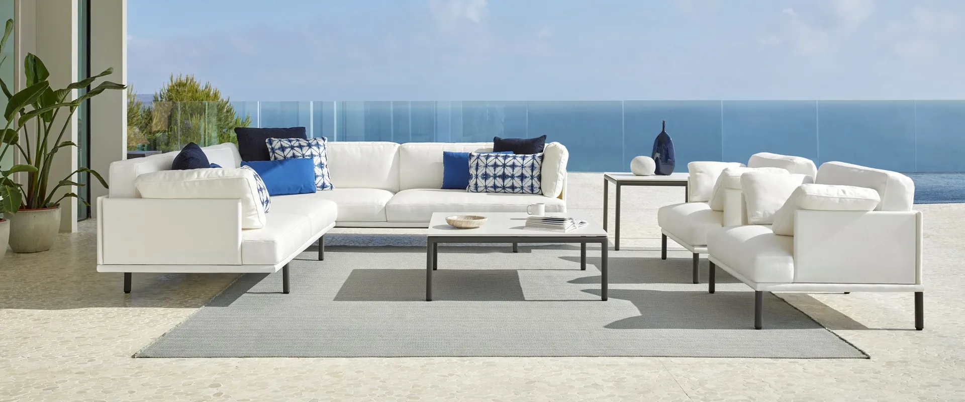 Point Long Island modular sofa in white with blue cushions under a white porch, with the sea and sky beyond