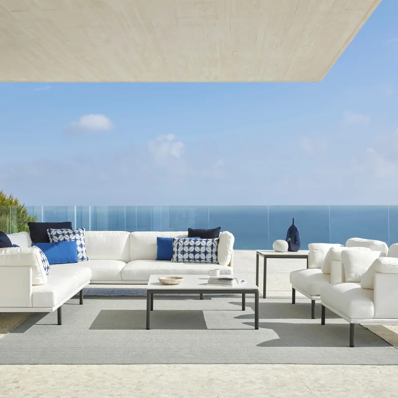 Point Long Island modular sofa in white with blue cushions on a terrace under a white canopy, the sea behind