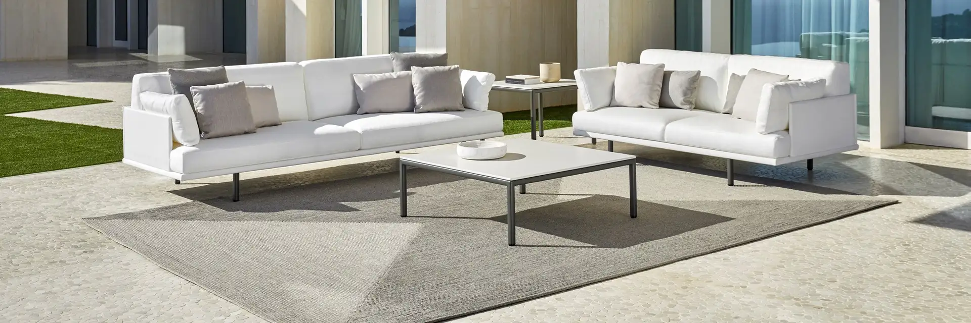 Point Long Island sofas and a low table on a rug on the terrace of a modern villa with tall glazing