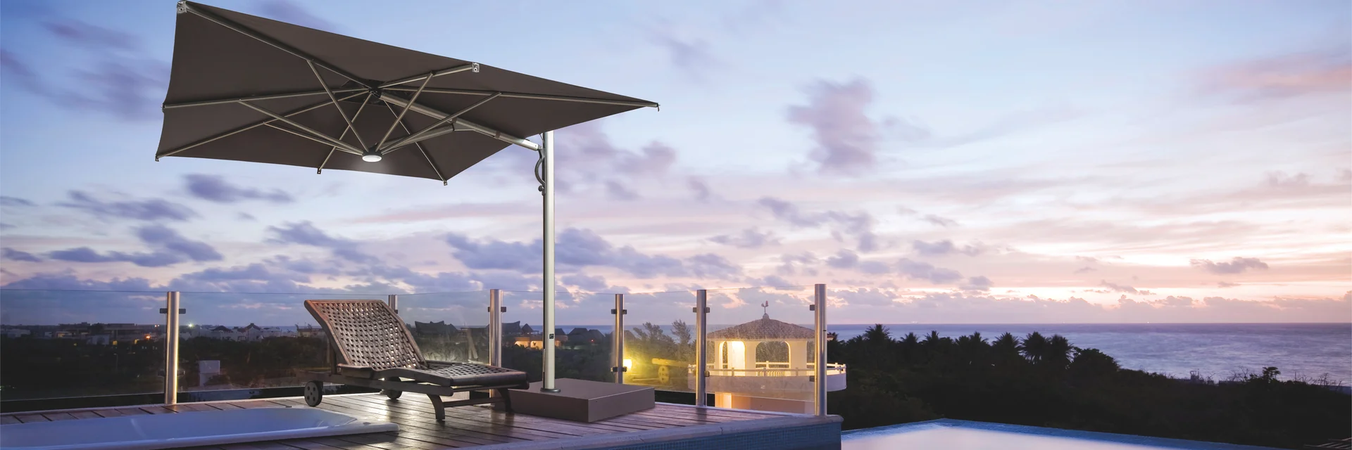 Dark Scolaro Galaxia Astro cantilever parasol with LED lighting over sun loungers beside an infinity pool overlooking the sea at dusk