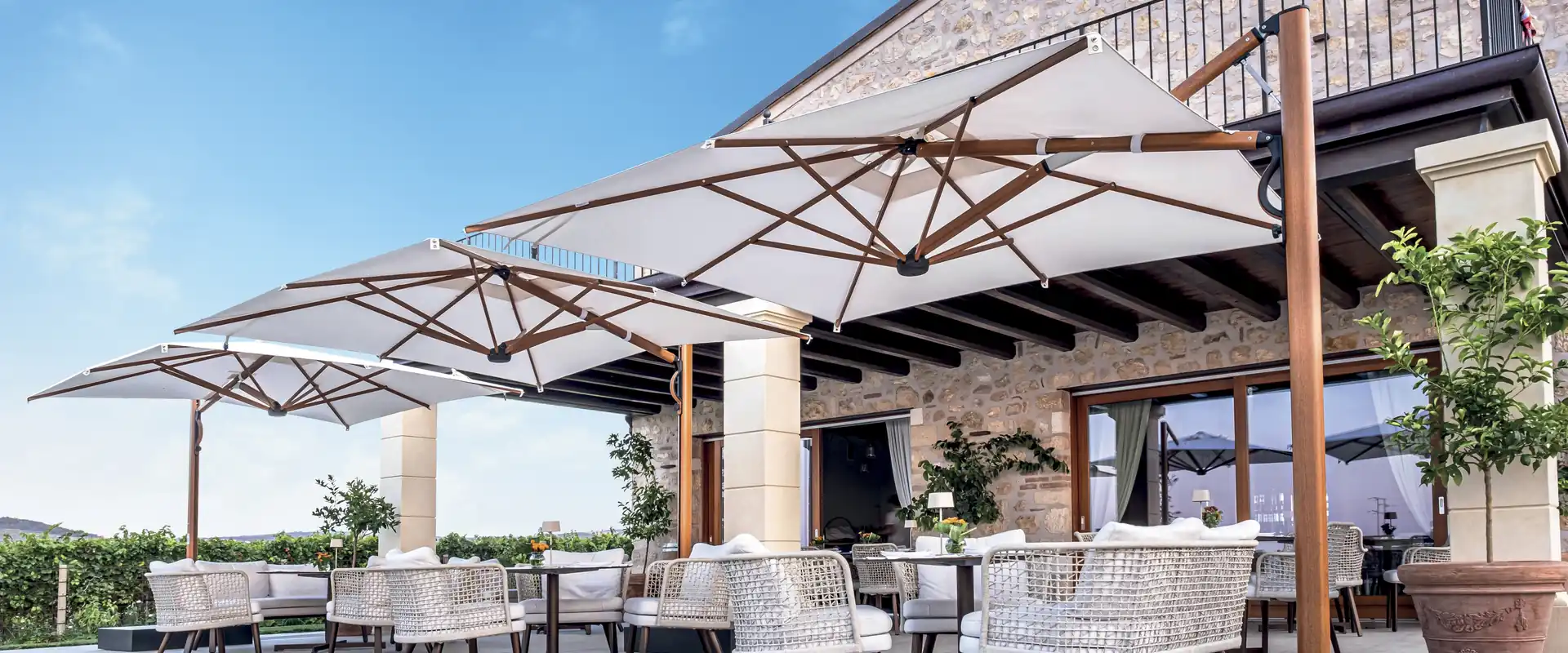 Scolaro Galaxia Astro parasols with timber ribs over the dining terrace of a stone country house