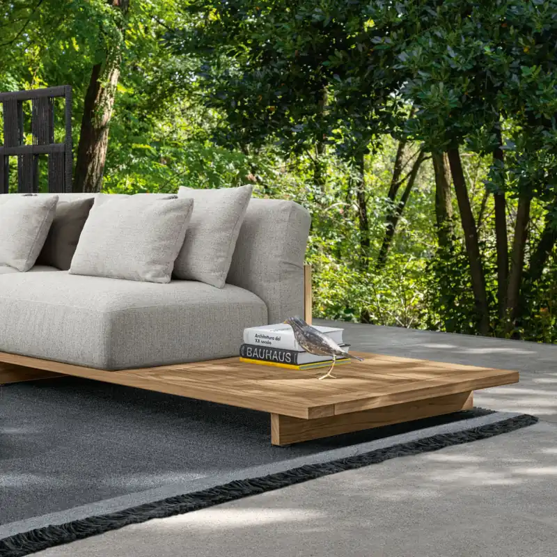 Talenti Argo sofa module on a low teak platform with gray cushions, on a deck among green trees