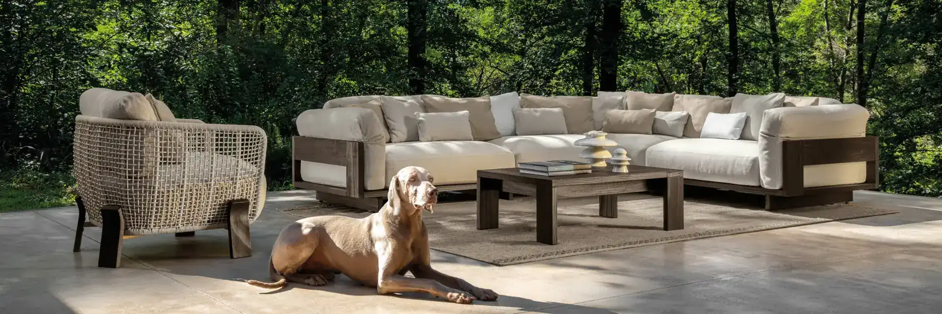 Talenti Argo modular sofa and a woven armchair on a terrace at the edge of a wood, with a dog lying in front