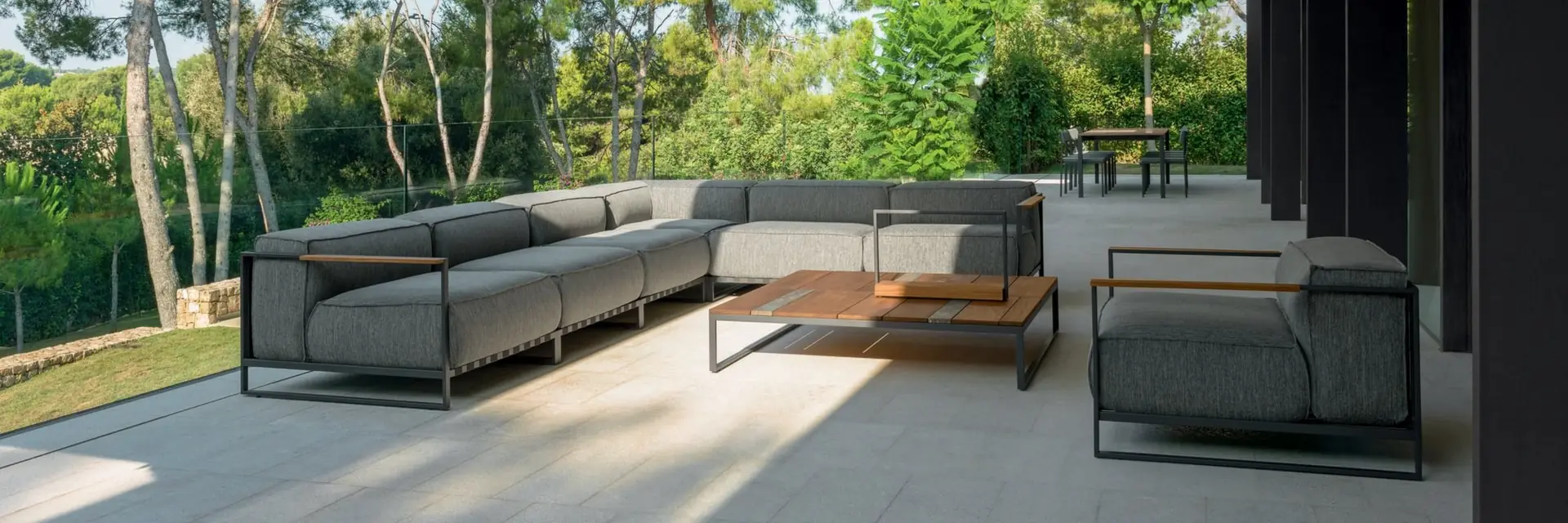 Talenti Casilda corner sofa and armchairs under a dark canopy opening onto a garden of pines