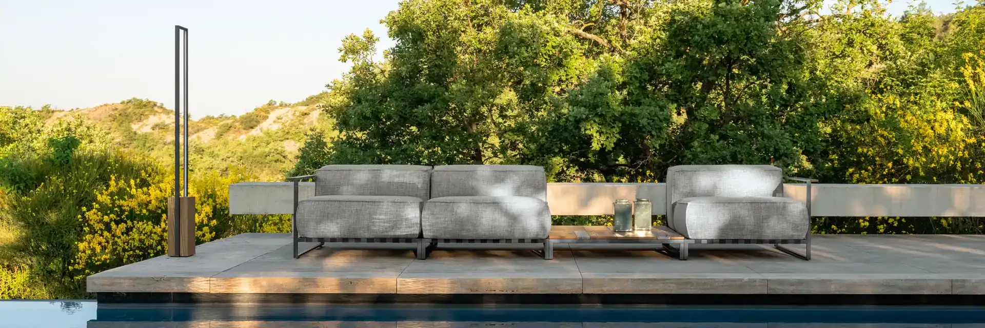 Talenti Casilda sofas on a deck at the edge of a still pool, with tall trees and hills behind
