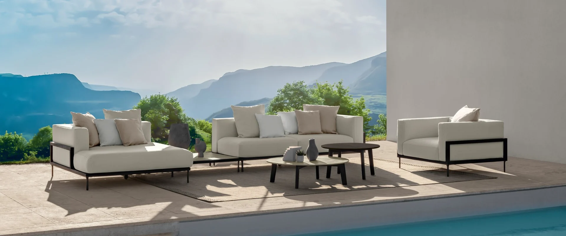 Talenti Cleo sofas and an armchair with dark frames on a poolside terrace overlooking the sea and a mountainous coast