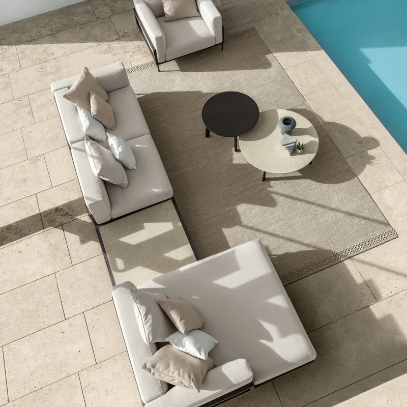 Talenti Cleo modular sofa, armchair and round tables on a stone terrace at the corner of a pool, seen from above